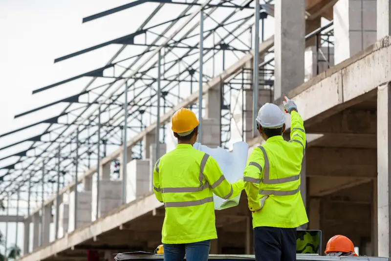 Construction professionals reviewing blueprints at a building site, emphasizing engineering and high technology in industrial sectors.
