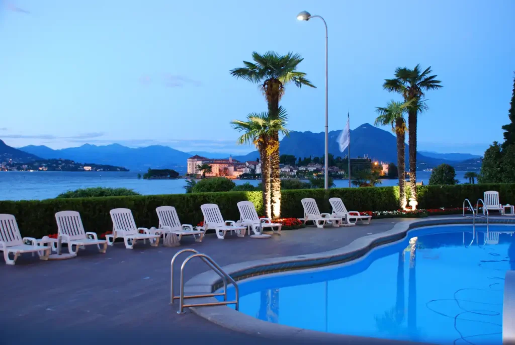 Poolside view of a serene lakeside hotel with palm trees, lounge chairs, and mountains in the background, emphasizing the hospitality and real estate sector.