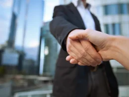 Business professionals shaking hands in front of modern office buildings, symbolizing partnership and collaboration in Italian business law and investment opportunities.