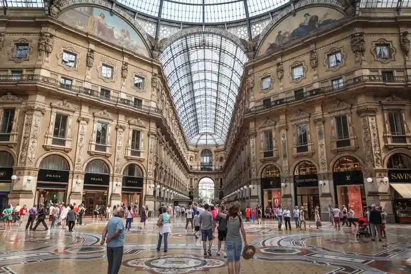 Galleria Vittorio Emanuele II in Milan, showcasing luxury shops like Prada and Louis Vuitton, with visitors exploring the ornate architecture and vibrant atmosphere.